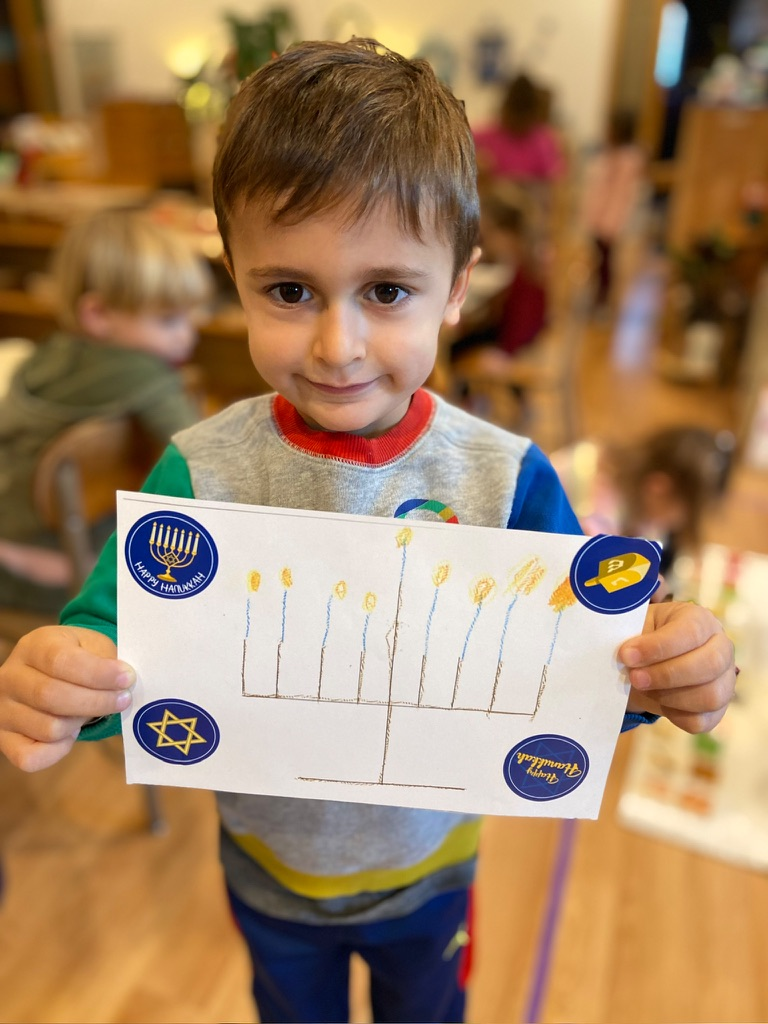 A boy holding up a colored pencil drawing of a lit menorah