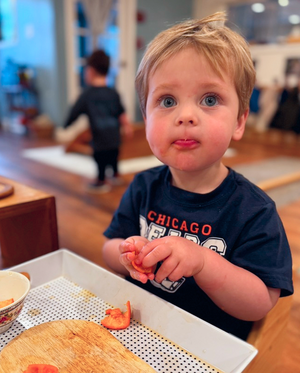 A young child eating small pieces of red pepper