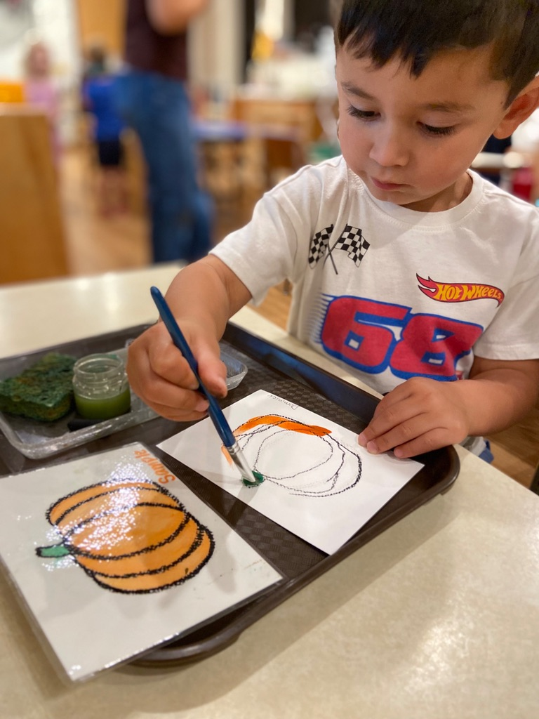 A child painting a picture of an orange pumpkin