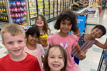 A group of children smiling in the aisle of a grocery store