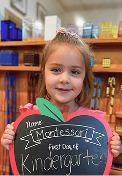 A smiling child holding a sign that says First Day of Kindergarten